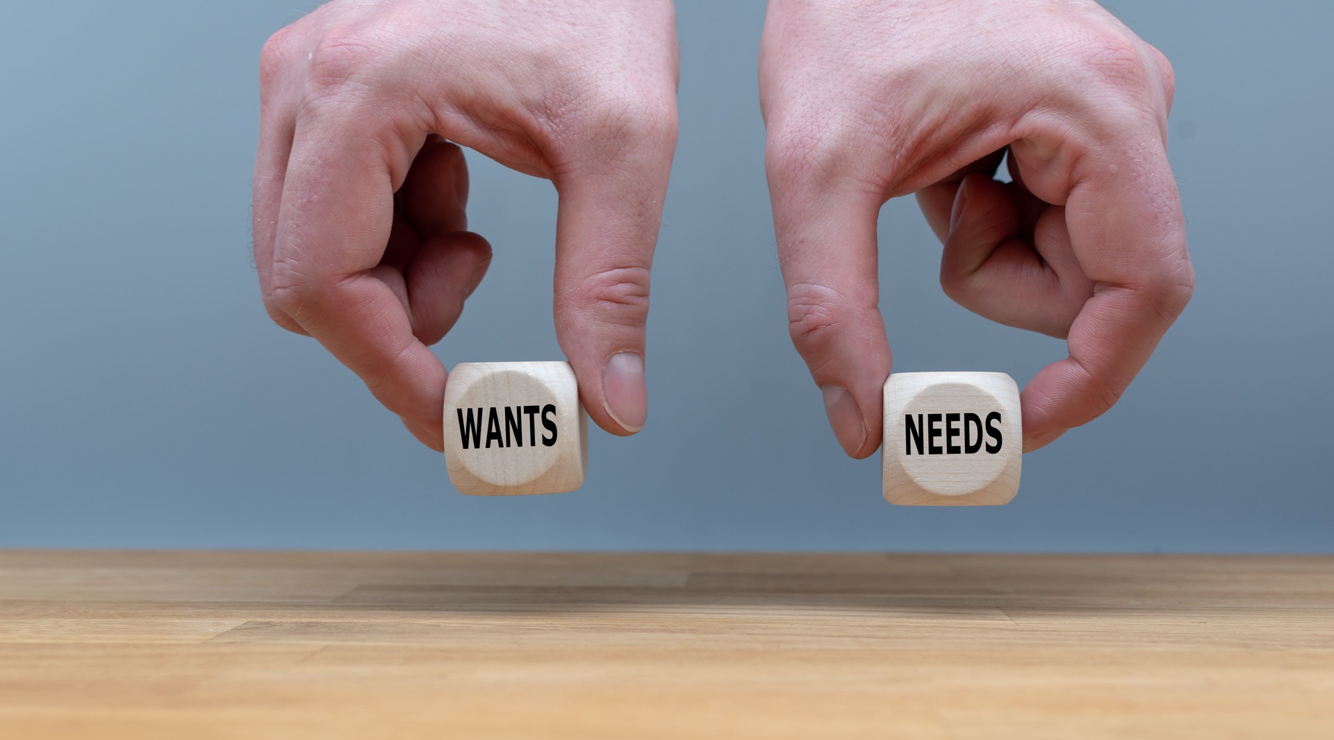 Two Hands hold two dice with the words "NEEDS" and "WANTS".